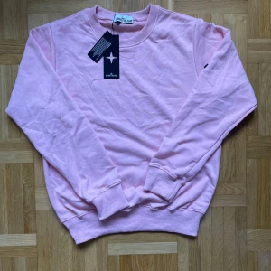 Stone Island crewneck rosa - Säljer en ljusrosa sweatshirt från Stone Island i mjuk bomull. Tröjan har rund hals, långa ärmar och klassisk passform. Medföljer ikonisk Stone Island-patch som kan fästas på ärmen. Perfekt för dig som gillar stilrena och trendiga plagg.