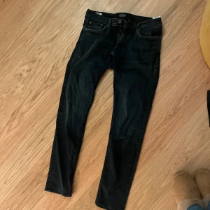 Svarta jeans Jack & Jones - Säljer ett par svarta jeans från Jack & Jones. Jeansen har klassisk femficksdesign, dragkedja och knapp framtill samt diskreta slitningar för en cool look. Materialet är stretchigt jeans för extra komfort och passform.