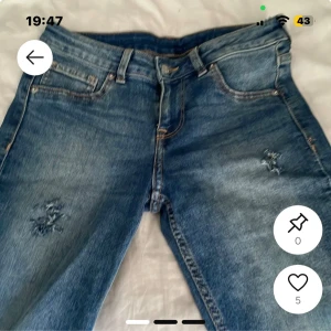 Blå jeans med slitningar - Säljer ett par klassiska blå jeans med snygga slitningar på båda benen. Jeansen har fem fickor, bälteshällor och dragkedjegylf. Perfekta för en avslappnad och trendig look.