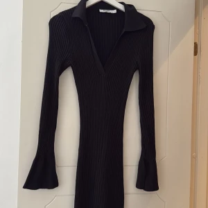 Svart ribbad långklänning från NA-KD - Svart långklänning från NA-KD med ribbad struktur, v-ringad krage och långa trumpetärmar. Klänningen har en figurnära passform och är tillverkad i ett stretchigt material som sitter snyggt på kroppen. Perfekt nu till hösten 🍁🍂😍
