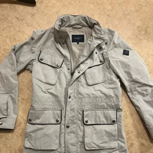 Beige vindjacka från Hackett - Snygg beige vindjacka från Hackett med svarta detaljer och fyra stora fickor framtill. Jackan har hög krage, dragkedja och tryckknappar. Perfekt för dig som vill ha en stilren och grym jacka inför hösten 🍂Bara kontakta för mer frågor och funderingar😁