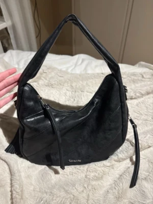 Handväska  - En Tamaris väska (ANNABELL) i svart. Köpt på Zalando, men finns ej i lager lägre. Ursprungspris 849 köpt för 594.  Höjd: 23 cm  Längd: 32 cm  Vidd: 10 cm  Handtag: 18 cm