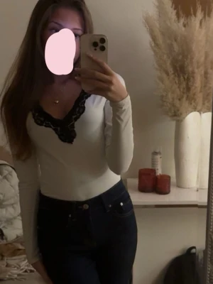 Vit långärmad topp med spets - Snygg vit långärmad body från H&M med v-ringning och svart spetsdetalj vid halsen. Perfekt att styla med jeans eller kjol. Enkel men ändå elegant design som lyfter din outfit.