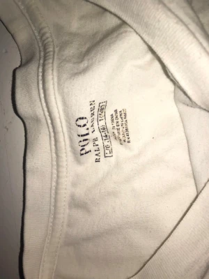 Vit långärmad topp från Polo Ralph Lauren - Vit långärmad topp från Polo Ralph Lauren med klassisk rund hals och diskret broderad logga i mörkblått vid nederkanten. Tillverkad i mjuk bomull som känns skön mot huden. Enkel och stilren design som funkar till många olika looks.