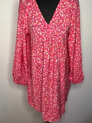 Blommig rosa kortklänning H&M XS - Supersöt kortklänning från H&M i storlek XS med blommigt mönster i rosa, vitt och orange. Klänningen har v-ringning, långa puffärmar med resår vid ärmslut och en luftig passform. Perfekt för vår och sommar! Aldrig använd