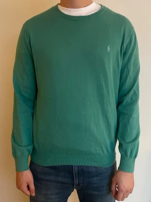 Tröja från Ralph Lauren - Säljer en grön tröja / turkos från Ralph Lauren med klassisk rund hals och diskret broderad logga på bröstet. Tröjan är i mjuk bomull och har ribbade muddar vid ärmslut och nederkant. Perfekt till jeans för en clean look.