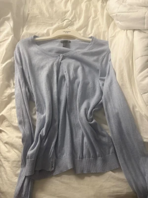 Ljusblå kofta från H&M Basic, storlek L - Säljer en ljusblå kofta från H&M Basic i storlek L. Koftan har rund halsringning, långa ärmar och knappar framtill. Materialet är mjukt och tunt, perfekt för lager-på-lager under vår och höst. Enkel och stilren design som funkar till många outfits.