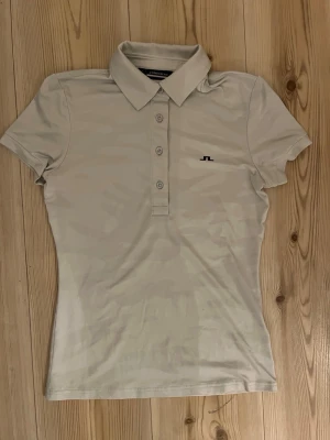 J.Lindeberg Alaya jacquard polo - XS - Säljer en stilren beige pikétröja från J.Lindeberg i storlek XS. Toppen har klassisk krage, korta ärmar och knappar framtill. Liten svart logga på bröstet och mjukt, stretchigt material som känns sportigt och fräscht.