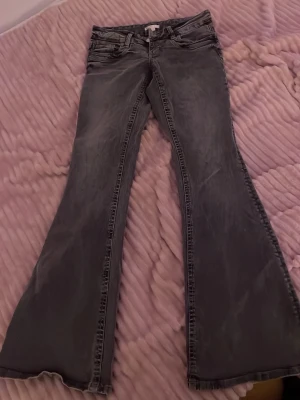 Bootcut grå jeans med utsvängda ben - Säljer ett par grå jeans med bootcut och riktigt utsvängda ben. Jeansen har klassisk bälteshällor och dragkedjegylf. Materialet är jeans och färgen är tvättad grå, vilket ger en cool vintagekänsla.
