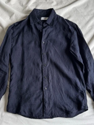 Premium linen shirt uniqlo  - Snygg mörkblå skjorta från Uniqlo i 100% linne. Klassisk krage, långärmad och med knappar framtill. Använd en gång