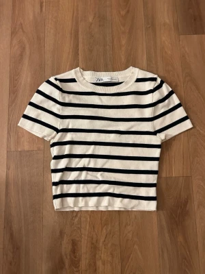Randig topp från Zara i bomull - Kortärmad topp från Zara i vit och svart med ränder. Modellen är croppad och har rund halsringning med ribbad kant. Tillverkad i mjuk bomull som känns skön mot huden. Perfekt för en enkel och stilren look.