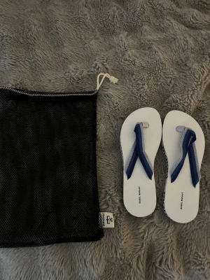 Isabel Marant vita sandaler med blå rem - Säljer ett par vita sandaler från Isabel Marant med breda remmar i blått och ljusblått. Sulan är vit med svart logga längs sidan och sandalerna kommer med en svart meshpåse. Perfekta för sommaren!! Nya och oanvända! Originalpris 1600.