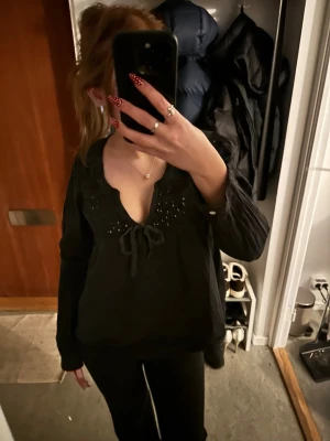 Blus - En super söt blus i svart. Som har massa fina unika små detaljer. Den har lite paljetter över bröstet och har en liten skärning med ett litet snöre som man knyter till en rosett. Sen har den dessutom två små super söta rosetter vid ärmarna och en liten knapp