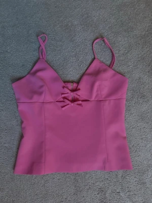 Rosa korsettopp med rosetter - Säljer en snygg rosa korsettopp med smala axelband och två dekorativa rosetter framtill. Toppen har en dragkedja i ryggen och är figurnära i modellen. Perfekt för dig som vill ha en feminin och trendig look.🩷❤️