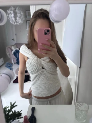 Vit omlott topp med twistad detalj - Säljer en unik vit topp med twistad omlott-design och struktur i materialet. Toppen har en asymmetrisk axel och sitter tight runt kroppen. Perfekt för dig som vill sticka ut med en cool och modern look.