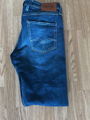 Replay blå jeans slim fit - Säljer ett par snygga blå jeans från Replay med klassisk femficksdesign och raka ben. Jeansen har ljusa slitningar framtill och bak, samt Replay-logga på bakfickan och läderpatch i midjan. Materialet är jeans med skön stretch och normal passform.