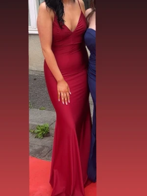Vinröd långklänning med smala axelband - Säljer en vinröd långklänning med smala axelband och djup v-ringning. Klänningen har en figurnära passform och är tillverkad i ett slätt, stretchigt material som ger en elegant siluett. Perfekt för bal eller festliga tillfällen. Använd en gång på min bal.
