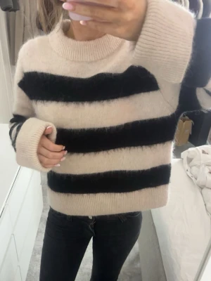 Randig fluffig stickad tröja - Supermysig stickad tröja med breda svarta och beige ränder. Tröjan har lång ärm, ribbade muddar och en lite lösare passform. 🤎🤍