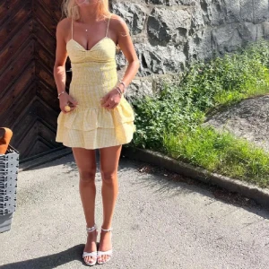 Gul kort sommarklänning med volanger - Supersöt gul och vit rutig kortklänning från Zara med smala axelband, volangkjol och söt rosett vid bysten. Klänningen har figurnära smockad midja och är perfekt för varma dagar. Lätt och luftig i bomullsmaterial.