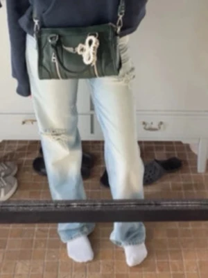 Ljusblå slitna jeans - Säljer ett par ljusblå jeans med slitningar på både lår och knän. Jeansen har en rak passform och klassisk femficksdesign. Materialet är jeans och de har en snygg, lite tvättad look som ger en avslappnad vibe.