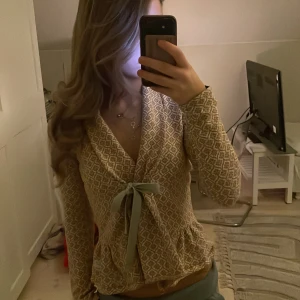 Mönstrad kofta från Odd Molly med rosett - Superfin beige och brunmönstrad kofta från Odd Molly med snygg knytrosett framtill. Koftan har lång ärm, v-ringning och ett unikt geometriskt mönster. Perfekt för lager-på-lager och ger en mysig men ändå chic vibe.