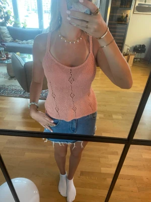 Stickad ljusrosa linnetopp - Säljer en stickad ljusrosa linnetopp med smala axelband och dekorativa hålmönster i diamantform längs framsidan och baksidan. Toppen har en mjuk, feminin look och är perfekt för varma dagar. Materialet känns luftigt och bekvämt mot huden.