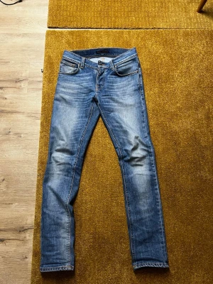 Nudie Jeans blå 28/32 - Säljer ett par sjyssta jeans från Nudie i storlek 28/32. Jeansen har rätt sjyssta slitningar och bra passform 