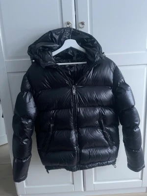 Svart pufferjacka från Zara, S - Säljer en svart pufferjacka från Zara i storlek S. Jackan har glansig finish, huva och dragkedja framtill. Perfekt för kalla dagar..Snygg och enkel att matcha med det mesta.