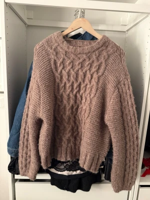 Beige stickad tröja från Vero Moda - Mysig beige stickad tröja från Vero Moda med grovt kabelstickat mönster och rund hals. Tröjan har långärmad passform och känns riktigt fluffig och varm, perfekt för kyliga dagar.