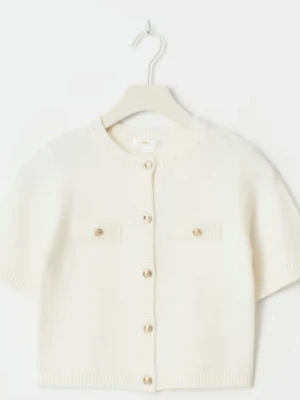 Vit kortärmad kofta med knappar - Kortärmad vit kofta med rund hals och dekorativa guldknappar framtill. Två små fickor på bröstet med matchande knappar. Ribbstickade detaljer vid ärmslut, hals och nederkant. Perfekt för en stilren och enkel look. Säljer denna för den är alldeles för liten. Och andvänd få tal gånger. 💗 