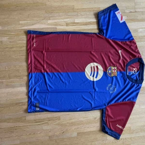 FC Barcelona Lamine Yamal matchtröja - Säljer en officiell FC Barcelona fotbollströja från Nike med Lamine Yamal och nummer 19 på ryggen. Tröjan har klassiska blå och vinröda fält, klubbmärke på bröstet och flera tryck. Tillverkad i lätt och ventilerande polyester.