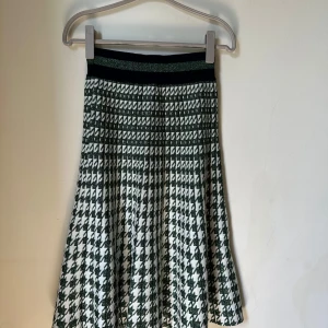 Grönvit rutig kjol Baum und Pferdgarten - Snygg grön och vit kjol från Baum und Pferdgarten med rutigt mönster och glittrig midjeresår. Kjolen är tillverkad av polyester och metallisk polyester med bomull i midjan. Den har en A-linjeformad siluett och är knälång, perfekt för att sticka ut.