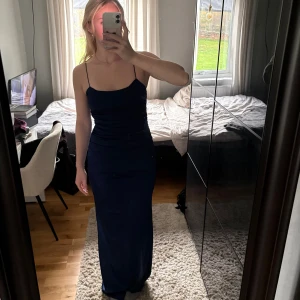 Marinblå långklänning med öppen rygg - Nypris 899 kr. Säljer en marinblå långklänning med smala axelband och snyggt åtsittande passform. Klänningen har öppen rygg med tunna band och en stilren, minimalistisk look. Perfekt för dig som vill sticka ut med en elegant och enkel stil. 