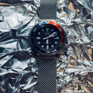 Seiko Diver Pepsi Bezel 34mm - Jag säljer denna Seiko 300 meter Diver klocka med en pepsi bezel. Denna klocka är äkta och är väldigt sällsynt. Den är vintage från 90 talet men i mycket bra skick som också bidrar till dens värde. En blå och röd bezel som är vridbar med solladdad urtavla som oftast lyser i mörkret pga hur mycket ljus den fått. 2 armband går med. Original armband- svart gummiarmband+silverarmband. Hör av dig vid minsta fråga! Är oftast öppen för pris. ☺️⌚️⏱️ Det är en man klocka men passar dam lika bra. 😊