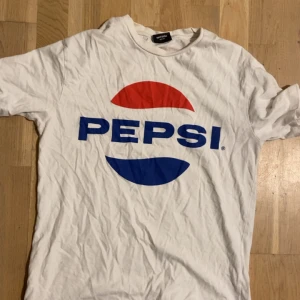 Vit Pepsi t-shirt från Sweet Sktsb - Vit t-shirt från Sweet Sktsb med stor Pepsi-logga i rött och blått framtill. Klassisk passform med rund hals och korta ärmar. Tillverkad i mjuk bomull, perfekt för en avslappnad streetstyle-look.