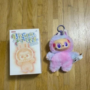 Labubu - Biginto Energy är en söt samlarfigur från Pop Mart, levereras med originalförpackning. Plyschfiguren har lila och rosa färger, stora ögon och ett mjukt yttre. Perfekt skick, ingen synlig skada eller slitage. Passar som dekoration eller nyckelring.