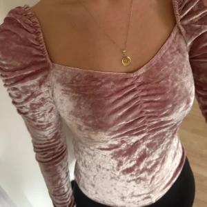 Rosa sammetstopp från Olé by Koton - Supersnygg ljusrosa topp i sammet från Olé by Koton. Toppen har långa puffärmar, fyrkantig ringning och rynkade detaljer framtill. Perfekt för dig som vill sticka ut med en mjuk och glansig look.