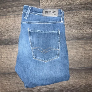 Replay Anbass hyperflex  - Snygga blå jeans från Replay Anbass Hyperflex med klassisk femficksdesign och diskreta slitningar. Jeansen har smal passform och raka ben, samt snygga detaljer på bakfickorna. Perfekta för dig som gillar en stilren och modern look. W33, L34. Midja 43cm, längd 107cm. JAG SKICKAR INGA FLER BILDER PÅ NÄR JAG BÄR PLAGGET:) OBS gylfen fungerar inte, se små knoppar på bild. S2