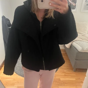 Svart teddyjacka (slutsåld på hemsidan) - Säljer en svart teddyjacka med oversized passform och bred krage. Jackan har en grov struktur med knappar som detalj. Perfekt för dig som gillar en chill och trendig look. Passar dig som vill ha en varm och fluffig jacka med cool vibe.