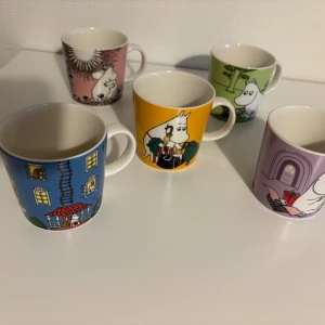 Muminmuggar samling (5 st) - Fem färgglada Muminmuggar från Arabia med olika motiv. Muggarna är i fint skick, men en mugg (rosa) har en liten defekt på kanten (se bild 3). Perfekt för samlare eller som present. Alla motiv är tydliga och muggarna är hela i övrigt. Skickar enbart med PostNord blåa paket.