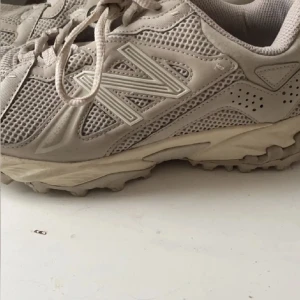 Beige sneakers från New Balance  - Säljer ett par snygga beige sneakers från New Balance. Skorna har en robust sula och klassisk snörning. Perfekta för en avslappnad stil och bekväma för långa promenader.