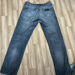 Wrangler Frontier raka jeans i ljusgrå färg - Klassiska jeans från Wrangler i mörkblå tvätt med raka ben och femficksdesign. Jeansen har normal passform och är tillverkade i slitstark bomullsdenim. Perfekta för dig som gillar en tidlös och avslappnad look.