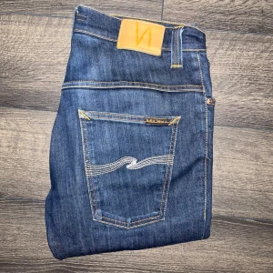 jeans Nudie  - Snygga mörkblå jeans från Nudie Jeans med klassisk femficksdesign och kontrastsömmar. Jeansen har raka ben och tydliga Nudie-detaljer på bakfickorna. Tillverkade i bomull för en skön känsla och stilren look. Midja 39cm, längd 106cm. JAG SKICKAR INGA FLER BILDER PÅ NÄR JAG BÄR PLAGGET :) s2