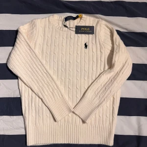 Vit kabelstickad tröja Polo Ralph Lauren - Vit kabelstickad tröja från Polo Ralph Lauren med klassisk rund hals och broderad logga på bröstet. Tröjan är långärmad och har ribbade muddar vid ärmslut och nederkant. Fungerar till alla klädstilar och till både killar och tjejer. OBS tröjan är lite liten i sin storlek. Därför jag säljer denna snygg tröjan. Skriv vid mer frågor eller bilder !!!!