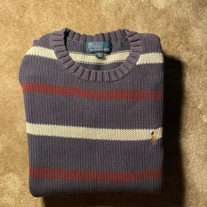 Randig Ralph lauren tröja - Snygg stickad tröja från Polo Ralph Lauren i marinblått med vita och vinröda ränder. Klassisk rund hals och ribbade muddar. Liten broderad logga på bröstet. Perfekt för dig som gillar preppy stil och vill ha något som sticker ut.                                          ⭐️skick: 8/10 mycket bra skick den har några små skråmor och lite små isärdragna hål,  🎲storlek:8-10 år 🎨färg:vit blå röd  📦: snabb och varsam frakt. 