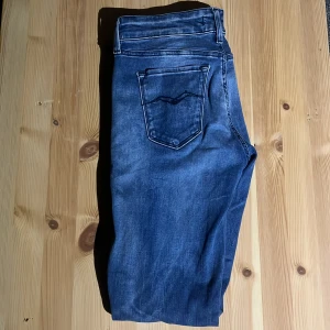 Blå jeans från Replay, midja 29/30 - Säljer ett par klassiska blå jeans från Replay med snygga slitningar och kontrastsömmar. Jeansen har fem fickor och en diskret Replay-logga vid fickan. Perfekt passform och tillverkade i mjukt denimtyg för en skön känsla.