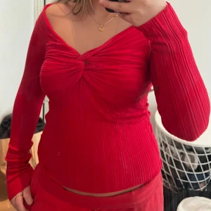 Röd ribbad långärmad topp med twist - Säljer en snygg röd ribbad topp med lång ärm och offshoulder-skärning. Toppen har en twist-detalj framtill perfekt för dig som vill sticka ut med färg och form.