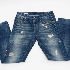 Blå slitna jeans från Jack & Jones - Snygga blå jeans från Jack & Jones med slitningar och lagade detaljer för en cool, avslappnad vibe. Klassisk femficksmodell med normal passform och raka ben. Jeansen har en ljus tvätt och tydliga slitningar både fram och bak.