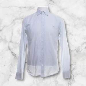 Ljusblå rutig skjorta Burberry S - Klassisk ljusblå och vit rutig skjorta från Burberry London. Skjortan har lång ärm, knappar framtill och en stilren krage. Tillverkad i 100% bomull för en skön och luftig känsla. Perfekt för dig som gillar en clean och tidlös look.