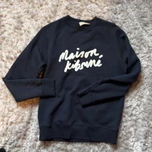 NYSKICK Maison Kitsuné mörkblå sweatshirt - NYSKICK - Aldrig använt. Snygg mörkblå sweatshirt från Maison Kitsuné med vit logotyp framtill. Klassisk rund halsringning och långa ärmar. Perfekt för dig som gillar stilrena och trendiga plagg med streetkänsla.